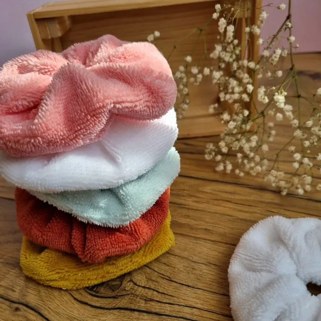 Lot de chouchous en éponge de bambou lavables et réutilisables, empilés sur un sol en bois. Accessoires capillaires doux et absorbants, parfaits pour attacher les cheveux sans les abîmer ou être portés au poignet pour absorber l’humidité lors de la routine beauté. Coloris variés – rose, blanc, bleu clair, terracotta et moutarde – pour s’adapter à toutes les envies. Fabrication artisanale et respectueuse de l’environnement.