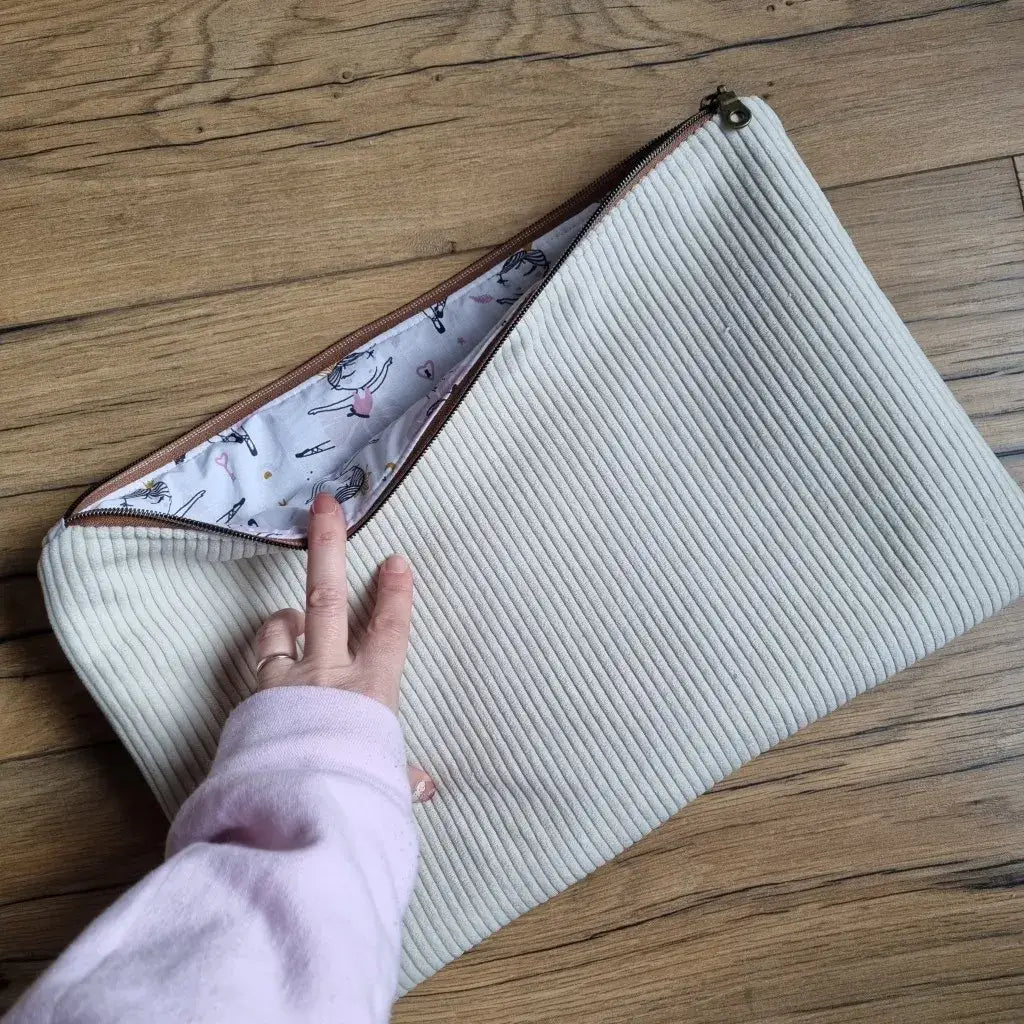 Housse d'ordinateur en velours côtelé écru, doublure illustrée ballerines, sur un parquet en bois.