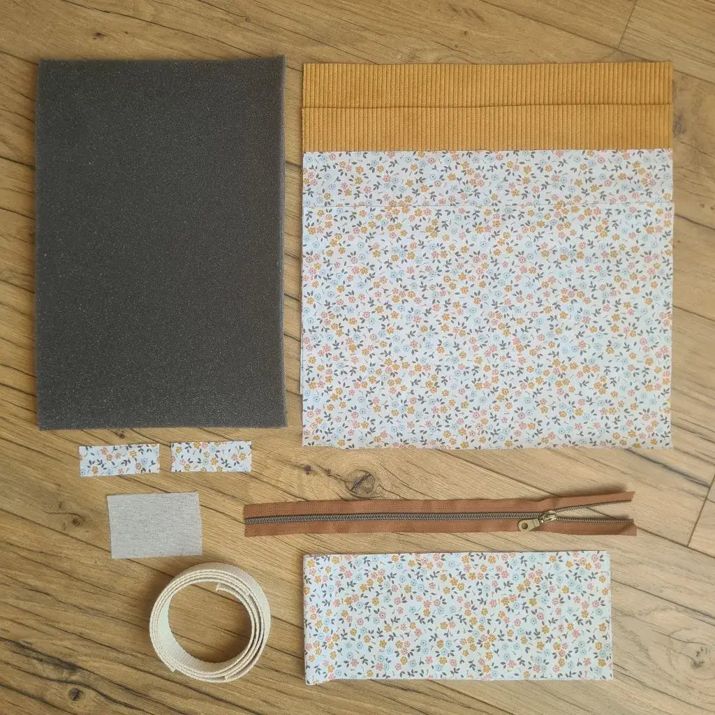 Kit "prêt à coudre" pour réaliser une housse avec anses pour tablette ou iPad en velours côtelé jaune doublée avec un tissu à motif fleurette. Ce kit couture est composé de 2 plaques en mousse, de 2 pièces en velours côtelé jaune, de 5 pièces en coton imprimé à motif fleurette, d'une fermeture éclair marron et de 2 sangles. La housse est personnalisable avec un prénom ou une inscription qui peut être floquée sur une étiquette en tissu coton et lin.