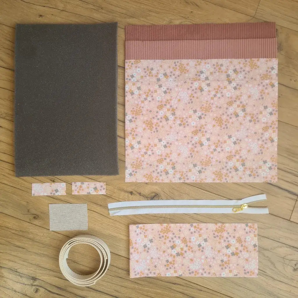 Kit "prêt à coudre" pour réaliser une housse avec anses pour tablette ou iPad en velours côtelé rose doublée avec un tissu à motif bouquet. Ce kit couture est composé de 2 plaques en mousse, de 2 pièces en velours côtelé rose, de 5 pièces en coton imprimé à motif bouquet, d'une fermeture éclair blanche et de 2 sangles. La housse est personnalisable avec un prénom ou une inscription qui peut être floquée sur une étiquette en tissu coton et lin.