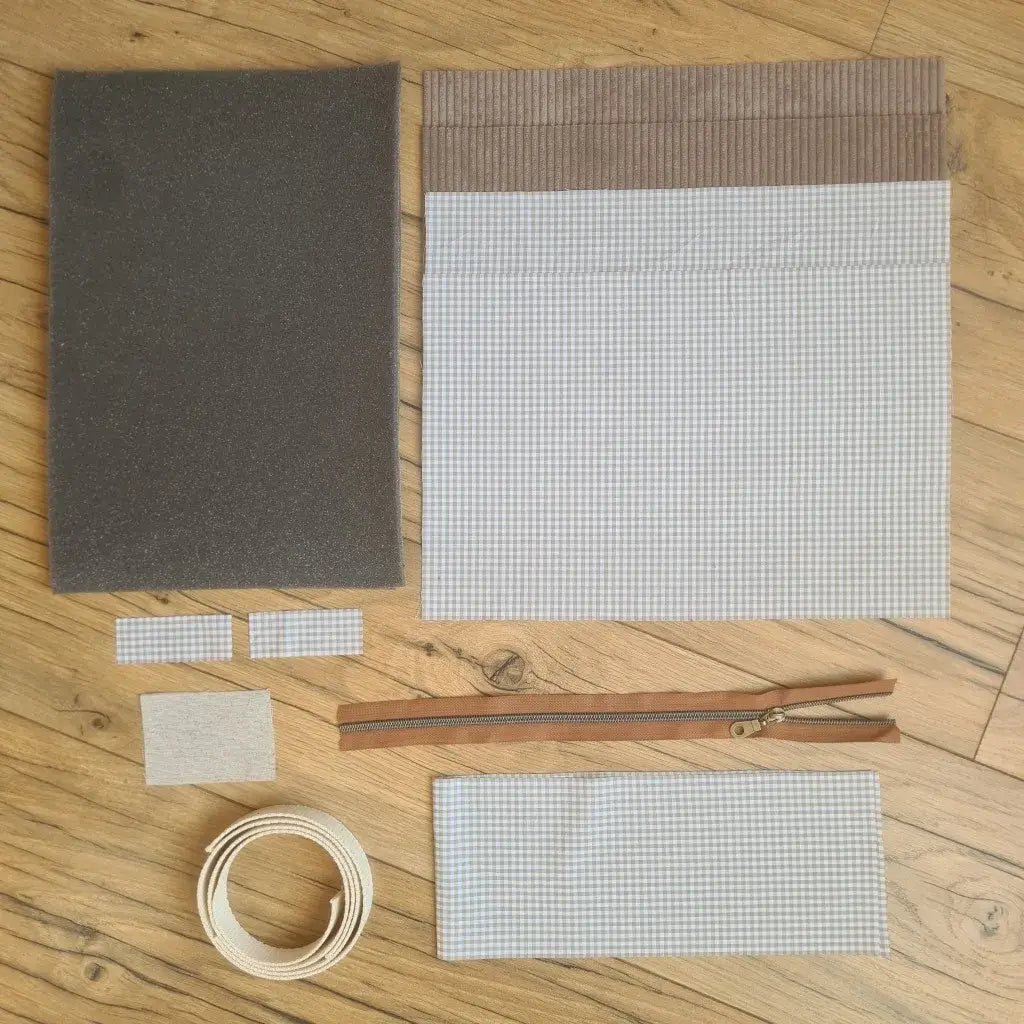 Kit "prêt à coudre" pour réaliser une housse avec anses pour tablette ou iPad en velours côtelé taupe doublée avec un tissu à motif carreaux beiges. Ce kit couture est composé de 2 plaques en mousse, de 2 pièces en velours côtelé taupe, de 5 pièces en coton imprimé à motif carreaux beiges, d'une fermeture éclair marron et de 2 sangles. La housse est personnalisable avec un prénom ou une inscription qui peut être floquée sur une étiquette en tissu coton et lin.