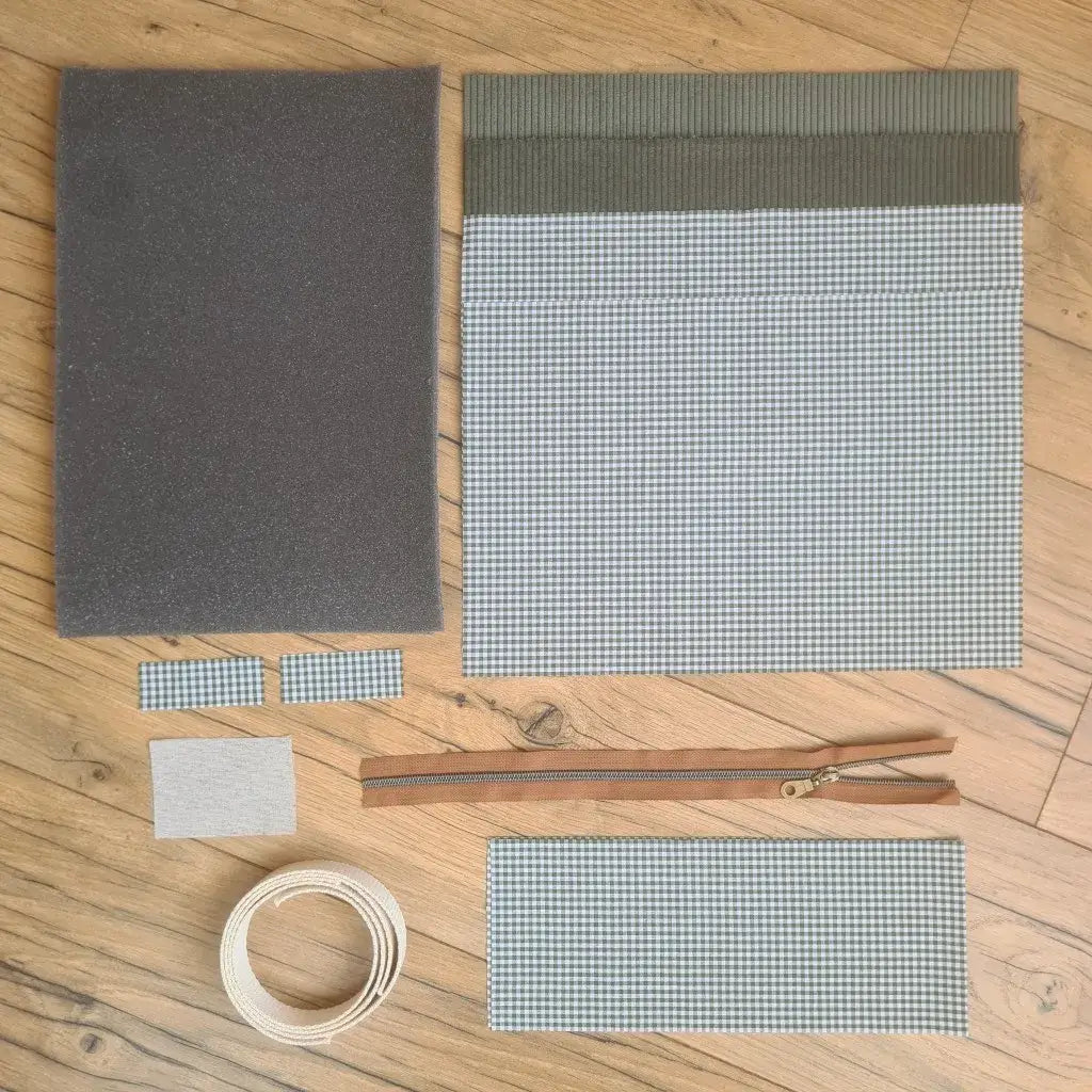Kit "prêt à coudre" pour réaliser une housse avec anses pour tablette ou iPad en velours côtelé vert doublée avec un tissu à motif carreaux verts. Ce kit couture est composé de 2 plaques en mousse, de 2 pièces en velours côtelé vert, de 5 pièces en coton imprimé à motif carreaux verts, d'une fermeture éclair marron et de 2 sangles. La housse est personnalisable avec un prénom ou une inscription qui peut être floquée sur une étiquette en tissu coton et lin.