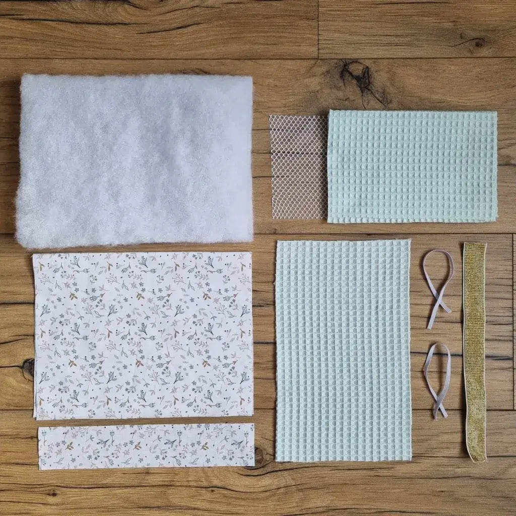 Kit "prêt-coudre" comprenant tous les éléments nécessaires pour confectionner une pochette de rangement multi-usages à rouler en nid d'abeille, molletonnée et doublée d'un tissu imprimé à motif. Le kit comprend un rectangle de ouate, 2 pièces en nid d'abeille (ici en coloris menthe), 2 pièces en coton imprimé (ici au motif azra), un filet, 2 élastiques fins et 1 élastique large (ici en coloris doré).