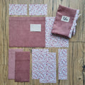 Kit prêt-à-coudre pour protège carnet de santé, comprenant des tissus prédécoupés en velours côtelé vieux rose et un imprimé floral délicat, présenté à plat sur un sol en bois. Accessoire DIY idéal pour confectionner un protège carnet unique et élégant. Modèle avec rabats et lien de fermeture, parfait pour organiser le carnet de bébé ou offrir un cadeau de naissance personnalisé. Kit complet avec toutes les pièces nécessaires pour une couture facile et un rendu soigné