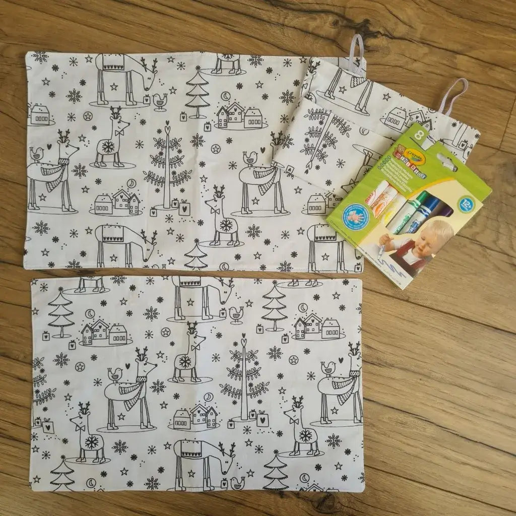 Lot de 2 set sde table en tissu à motifs à colorier recto et verso présentés avec leur trousse à rouler en tissu assorti ainsi qu'une boîte de 8 feutres à l'eau. Le modèle présenté ici est au motif "Noël".