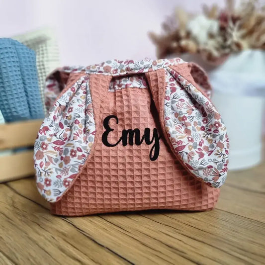 Panier de Pâques molletonné en tissu nid d'abeille de coloris marsala et doublé d'un tissu en coton imprimé à motif liberty. Ce panier de Pâques est personnalisé avec le prénom "Emy" floqué en noir sur le devant. Deux oreilles de lapin sont rabattues sur le panier.