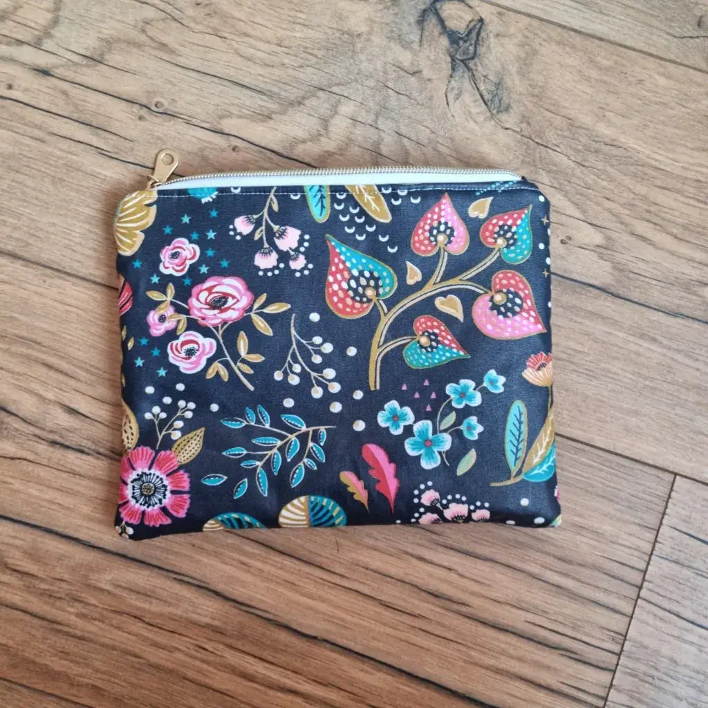 pochette zippée coton enduit bleu nuit avec motif floral coloré posée sur parquet bois