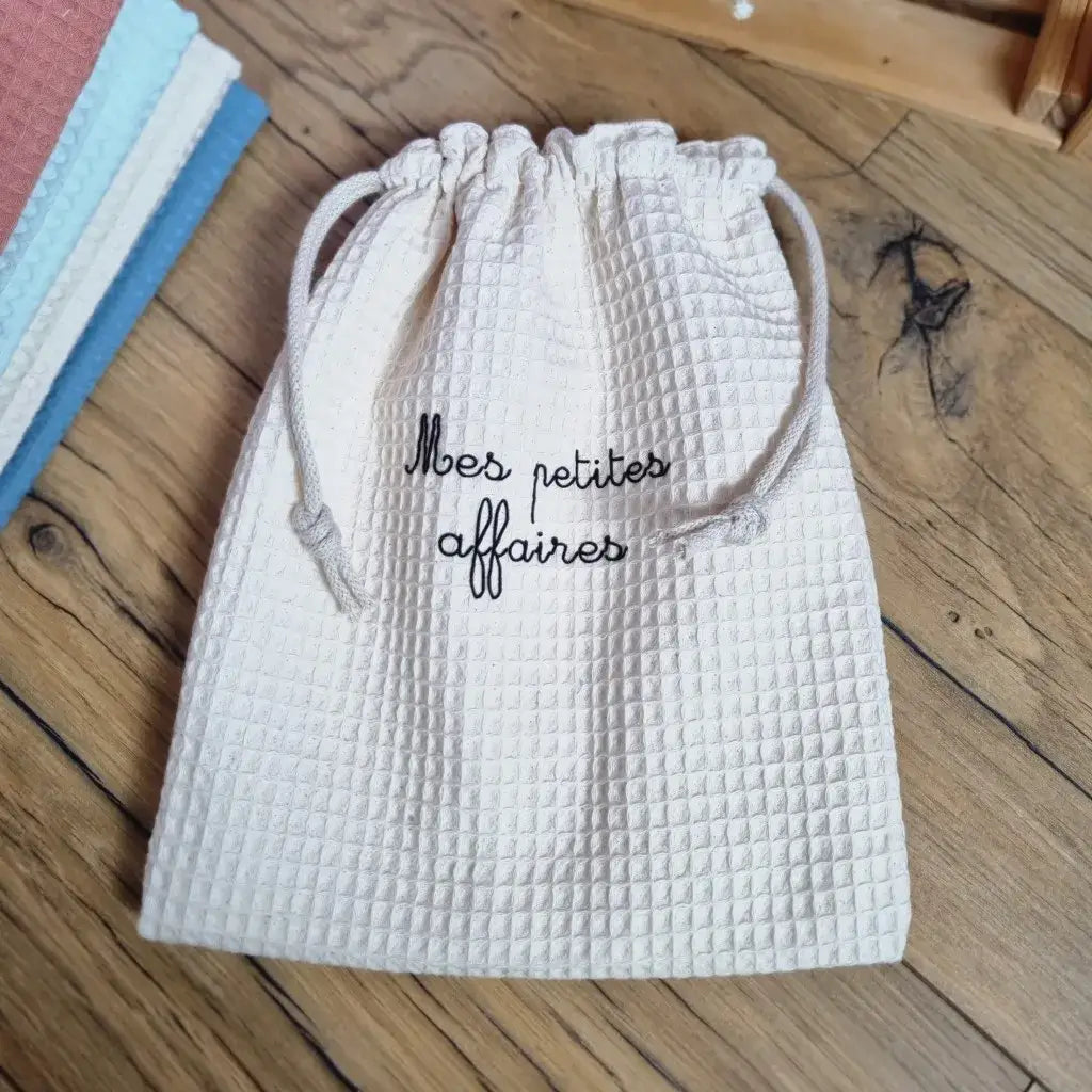 Pochon en tissu nid d’abeille au coloris naturel, doublé, avec inscription personnalisée 'Mes petites affaires', muni d’un cordon de serrage en coton. Sac de rangement lavable, idéal pour les accessoires de bébé ou les essentiels du quotidien.