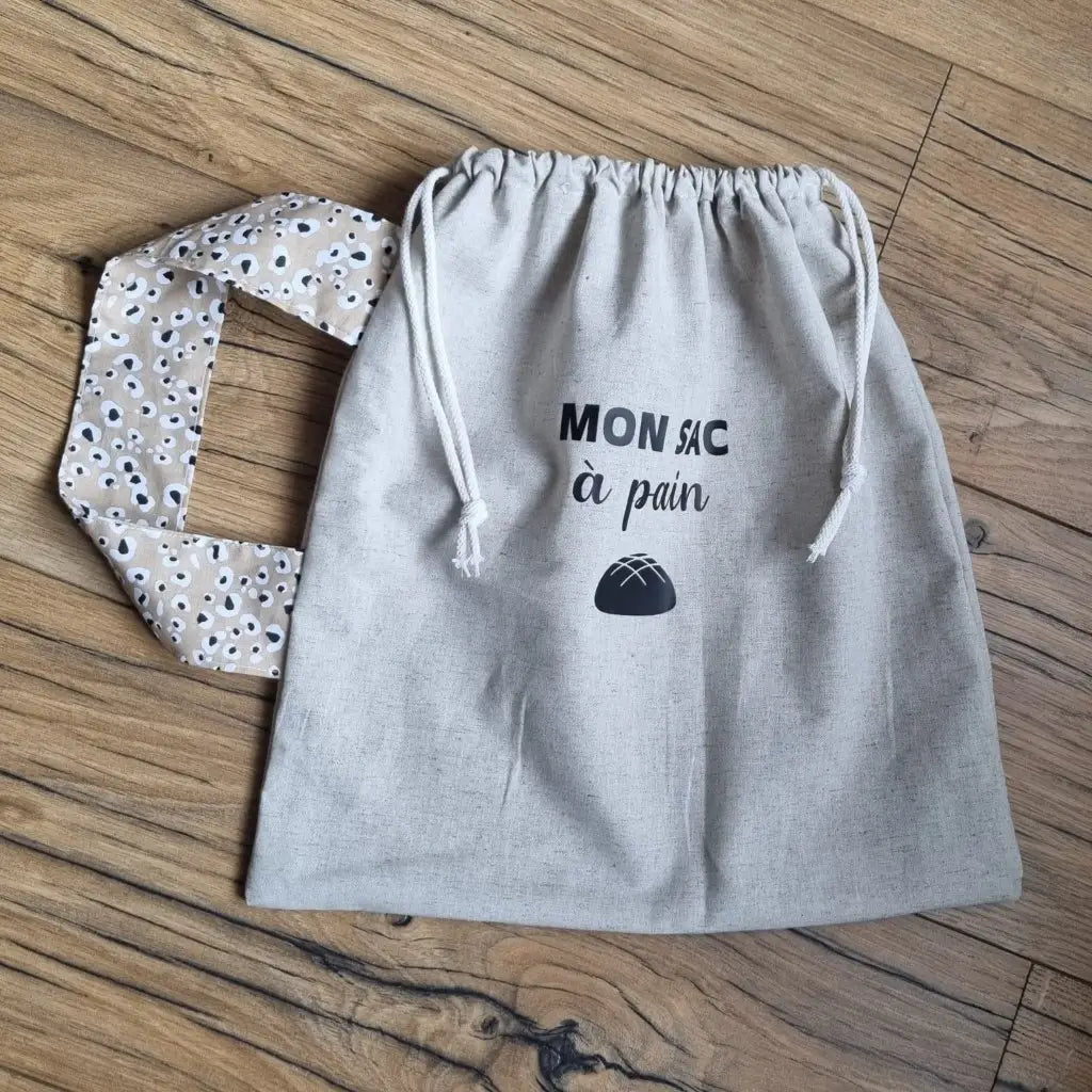 Sac à pain en coton au format miche se fermant par deux petites cordelettes blanches avec une sangle au motif léopard et l'inscription "Mon sac à pain" et le logo d'une miche de pain floqués au centre sur la partie supérieure haute.