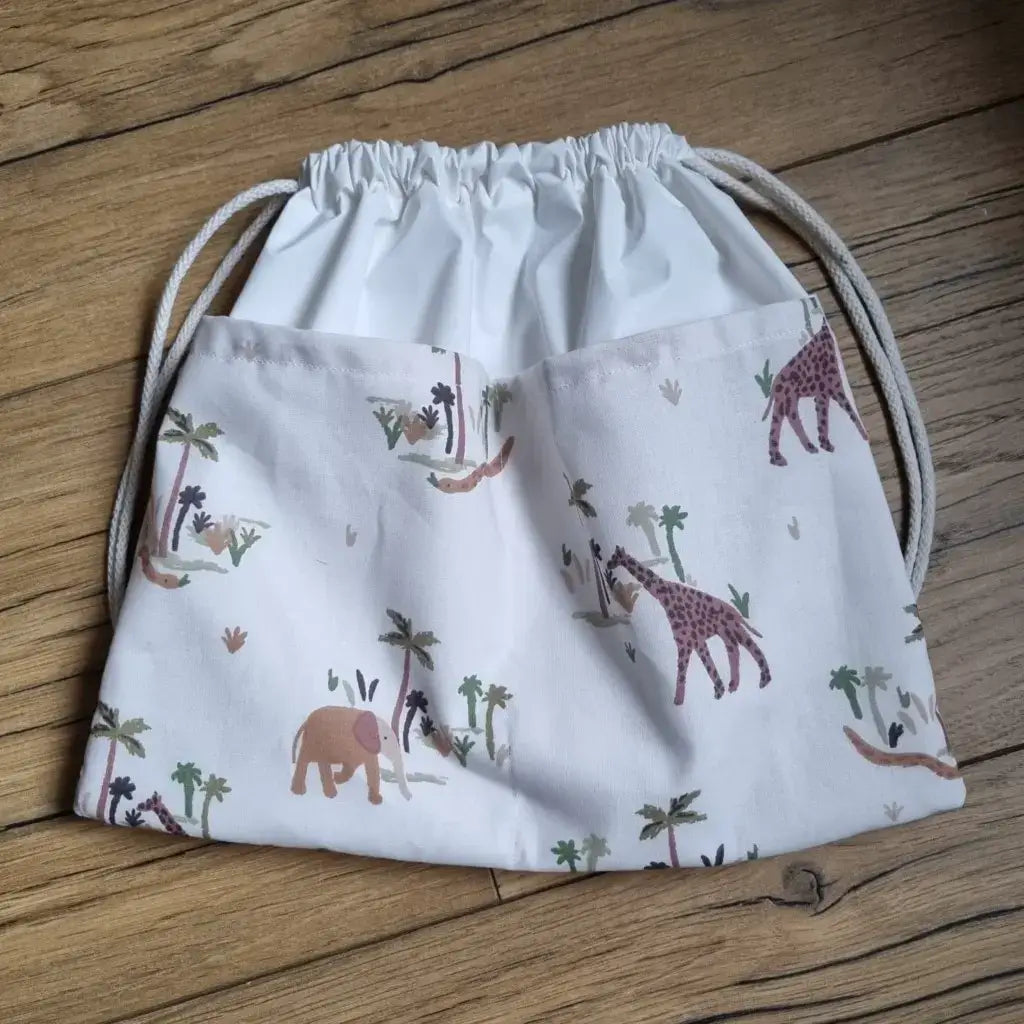 Sac piscine imperméable au format pochon se fermant grâce à deux cordelettes en coton blanc de part et d'autre et cousu avec un tissu imprimé à motif des animaux de la jungle comme des éléphants, des girafes, des serpents, ....