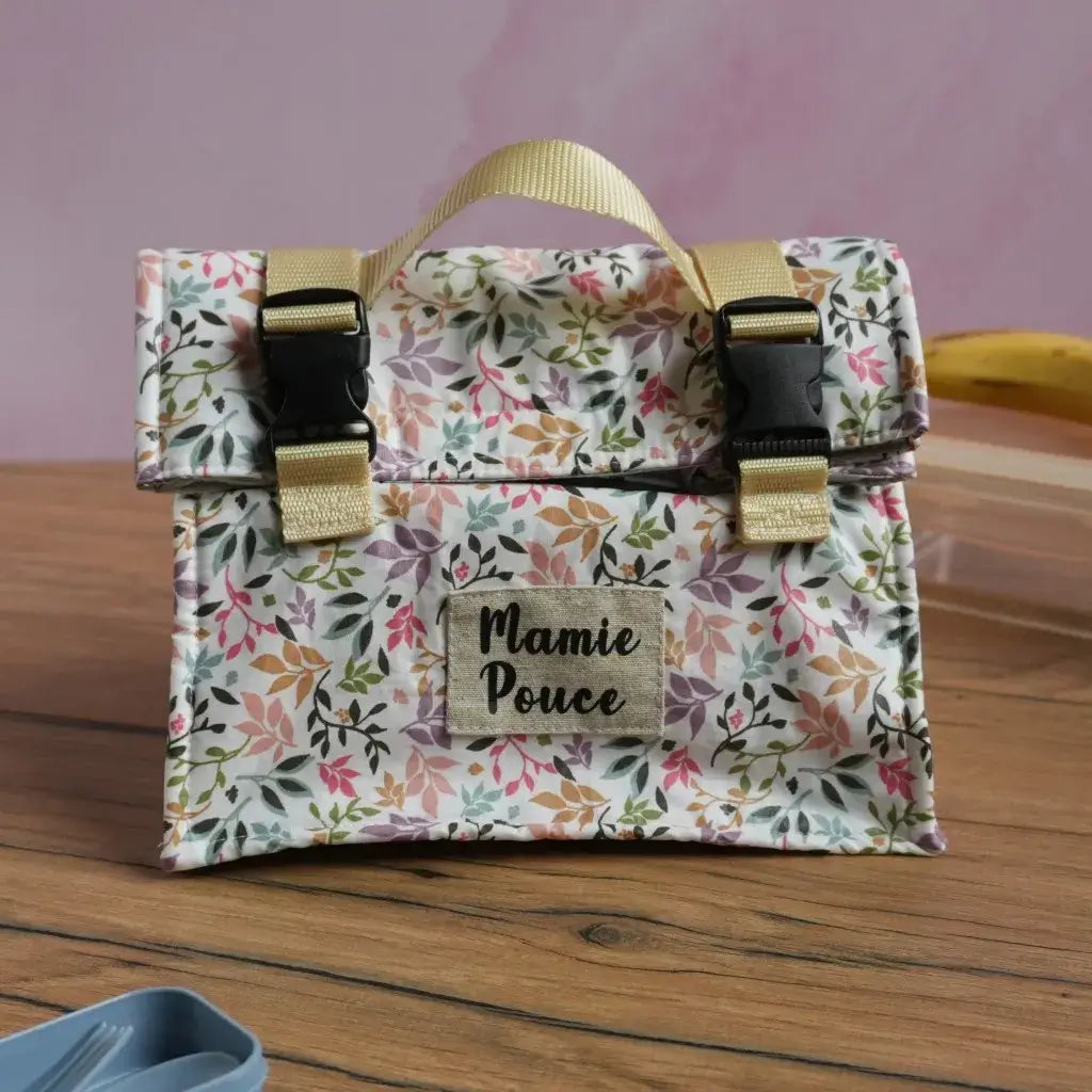 Sac repas isotherme personnalisé en coton enduit motif fleuri pastel avec inscription "Mamie Pouce" floquée en noir sur une étiquette, équipé de sangles beige et de fermetures à clips noirs. Lunch bag réutilisable et lavable, parfait pour transporter déjeuner ou goûter au bureau, à l’école ou en pique-nique avec style.