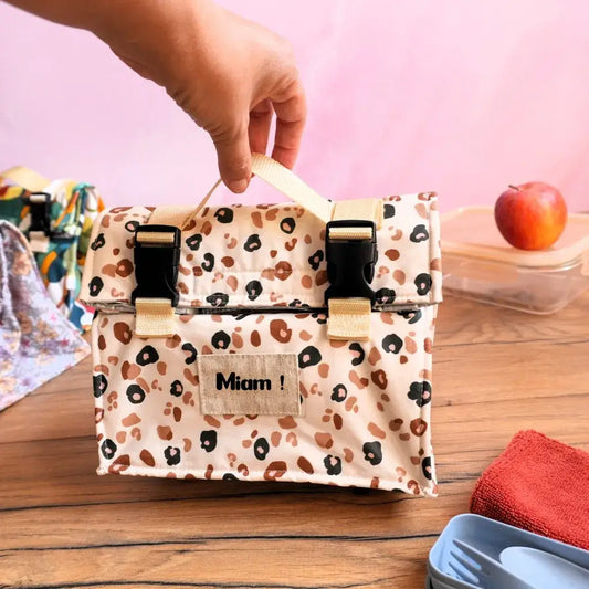 Lunch bag isotherme en coton enduit à motif léopard beige et marron, muni d’une poignée solide et de fermetures à clips pratiques, idéal pour conserver le repas au frais ou au chaud. Sac repas réutilisable et personnalisable avec l’inscription “Miam !”, parfait pour le bureau, l’école ou les pique-niques, alliant style tendance, praticité et engagement éco-responsable.