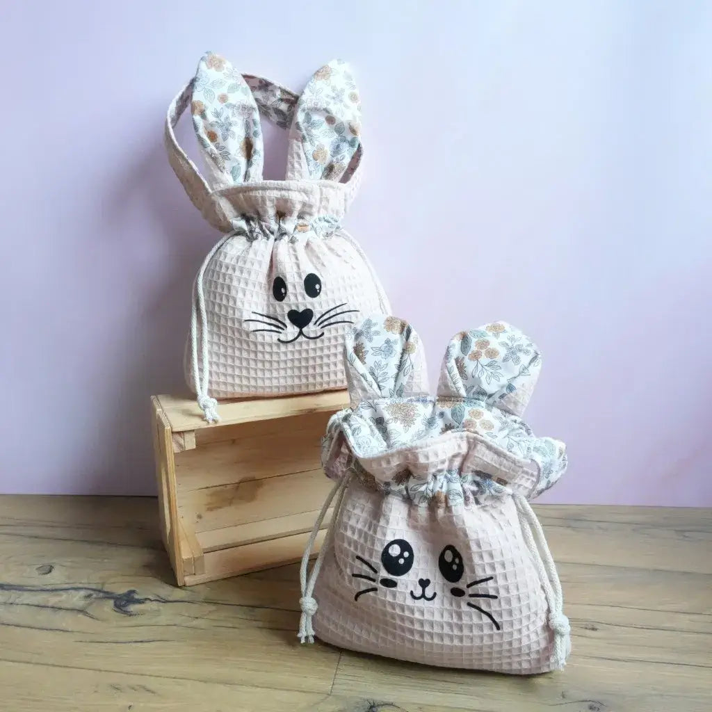 Deux pochons "Lapinou" et "Chatoune" en tissu nid d'abeille coloris peau avec oreilles fleuries, posés sur une caisse en bois.