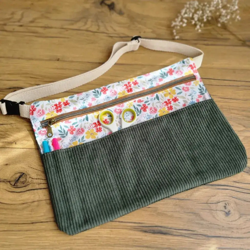 Tablier ceinture en velours côtelé vert foncé et coton imprimé fleuri multicolore, équipé d'une fermeture éclair dorée, de plusieurs poches de rangement et d’une sangle réglable en coton écru. Idéal pour les créatrices, couturières, animatrices ou professeures. Ce modèle pratique et élégant permet de garder ciseaux, stylos, épingles et accessoires toujours à portée de main. Parfait pour une utilisation quotidienne en atelier, en classe ou lors d'activités manuelles.