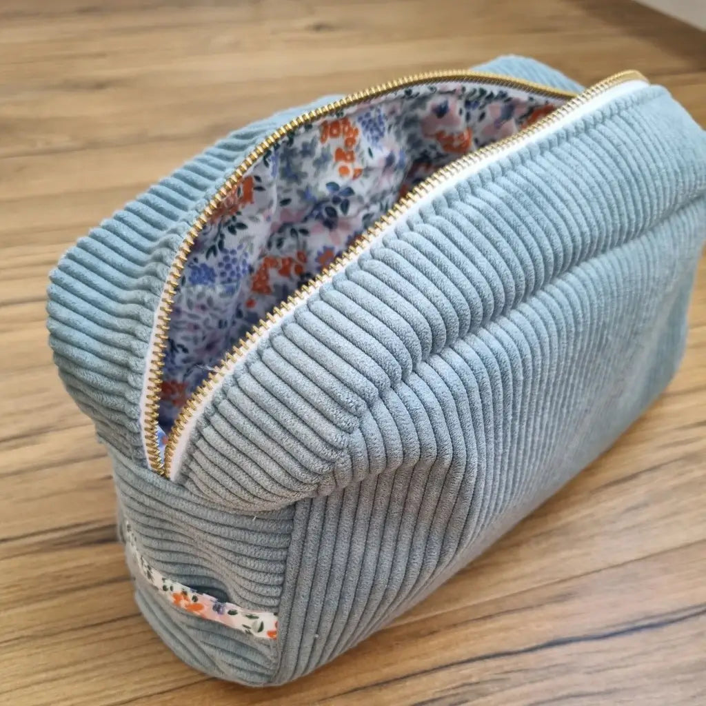 Trousse de toilette en velours côtelé bleu clair avec son zip ouvert laissant apparaître un tissu intérieur au motif fleuri.