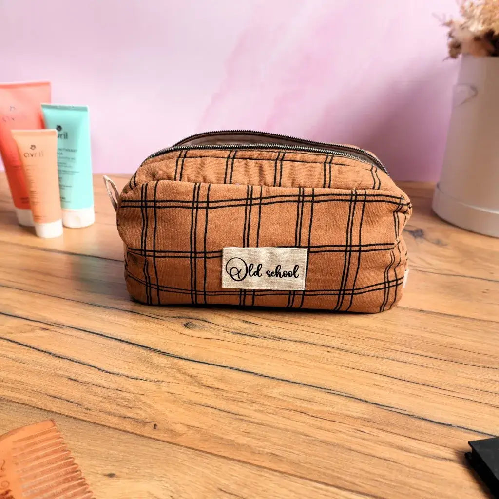 Trousse de toilette rectangulaire en tissu marron à carreaux noirs, avec inscription « Old school », posée sur une table en bois. Pratique et élégante, elle convient comme trousse de maquillage, pochette de voyage ou rangement beauté. Idéale pour emporter vos produits cosmétiques et soins avec style partout où vous allez.