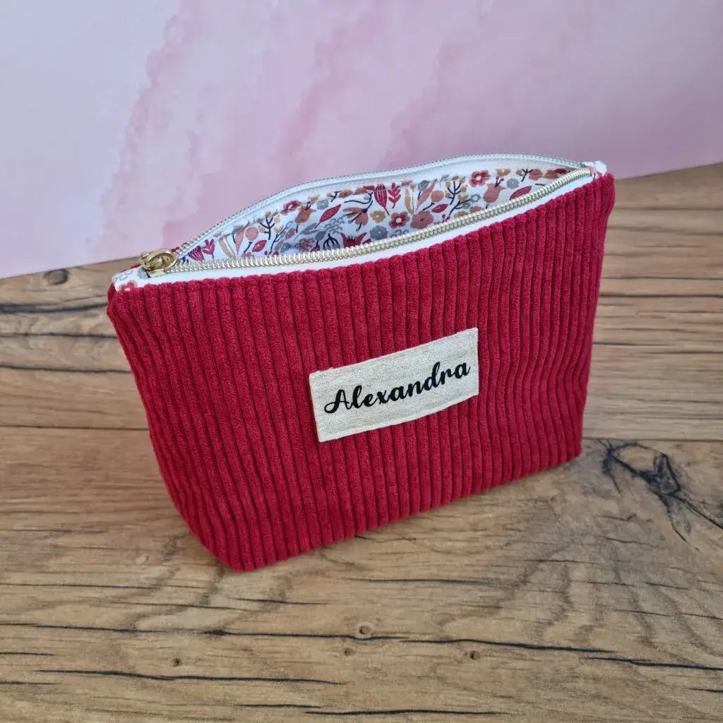 Trousse en velours côtelé bordeaux personnalisée Alexandra, doublure fleurie et zip doré sur fond bois.