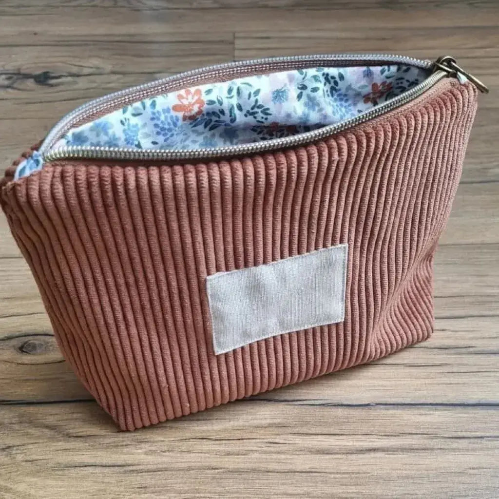 Trousse zippée en velours côtelé marron avec une doublure intérieure en coton imprimé à motif fleuri. Cette trousse dispose d'une étiquette en tissu cousue en façade pouvant accueillir un prénom ou une inscription personnalisée qui sera floquée dessus.
