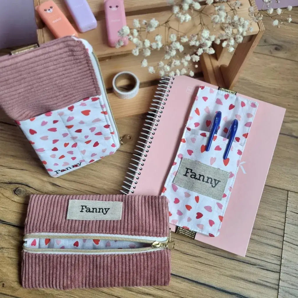 Lot de 3 trousses élastiques personnalisées pour carnet A5 – floquées au prénom ‘Fanny’ en velours côtelé rose et tissu à motifs cœurs, comprenant une trousse en velours rose avec zip central, un étui à stylos en tissu motif cœurs et une trousse velours et tissu avec fermeture éclair latérale, parfaits pour organiser ses fournitures scolaires avec douceur et style.