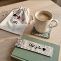 Marque-page fleuri bleu et rose « Chut, je lis » sur un livre vert, avec tasse de café sur un dessous de tasse assorti