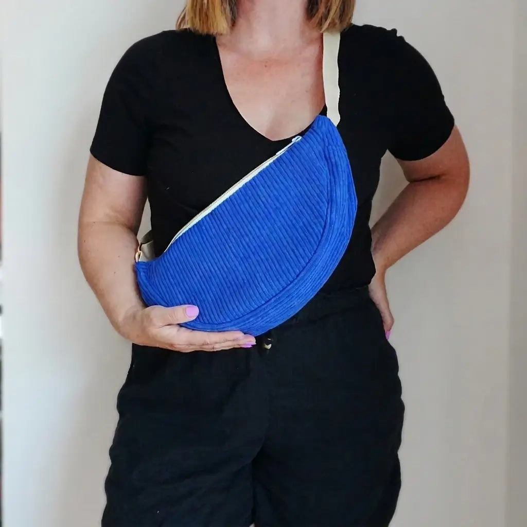 Sac banane bleu roi en velours côtelé porté en bandoulière, sangle écrue et zip diagonal