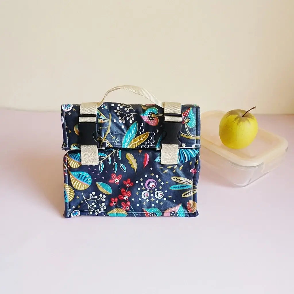 Sac repas bleu nuit à motif floral coloré, sangles à clips, présenté avec une boîte tupperware et une pomme