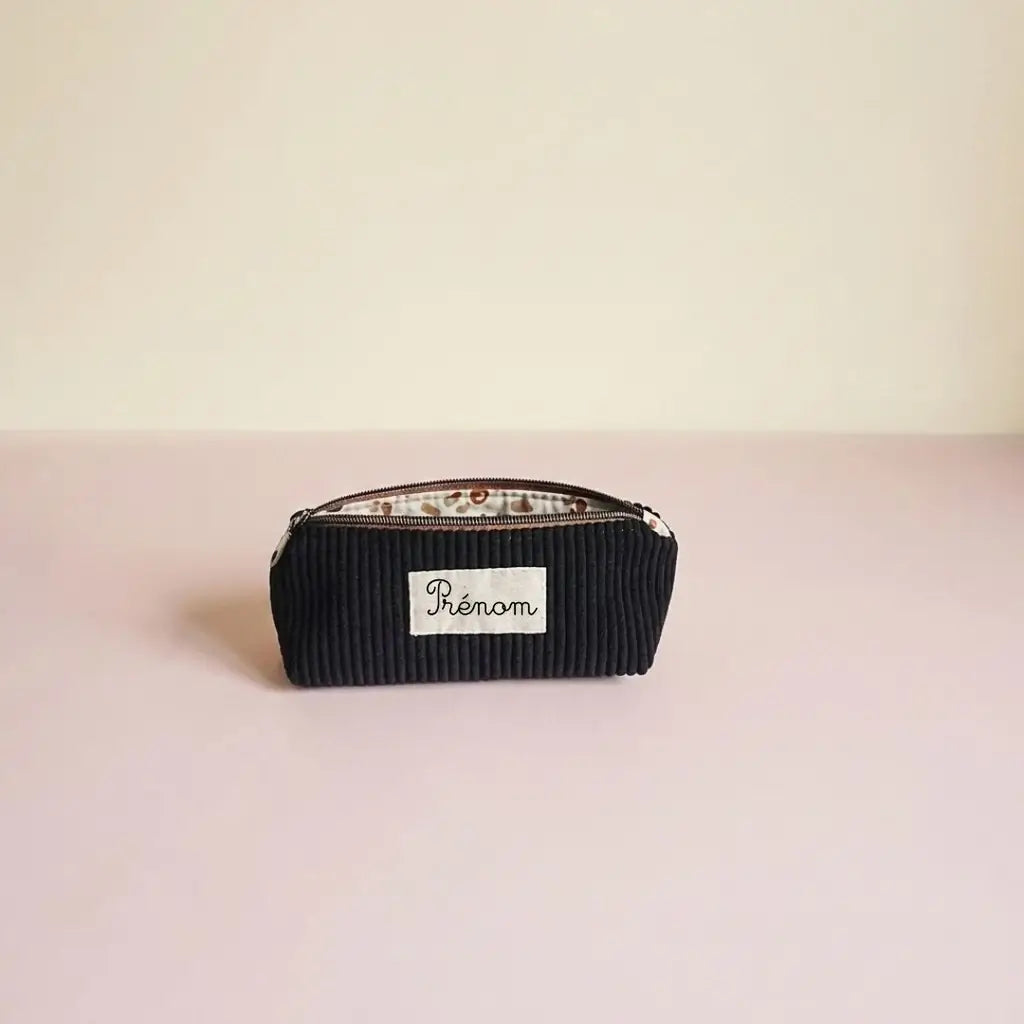 Trousse d'école noire en velours côtelé, doublure claire à taches brunes et étiquette prénom sur la face