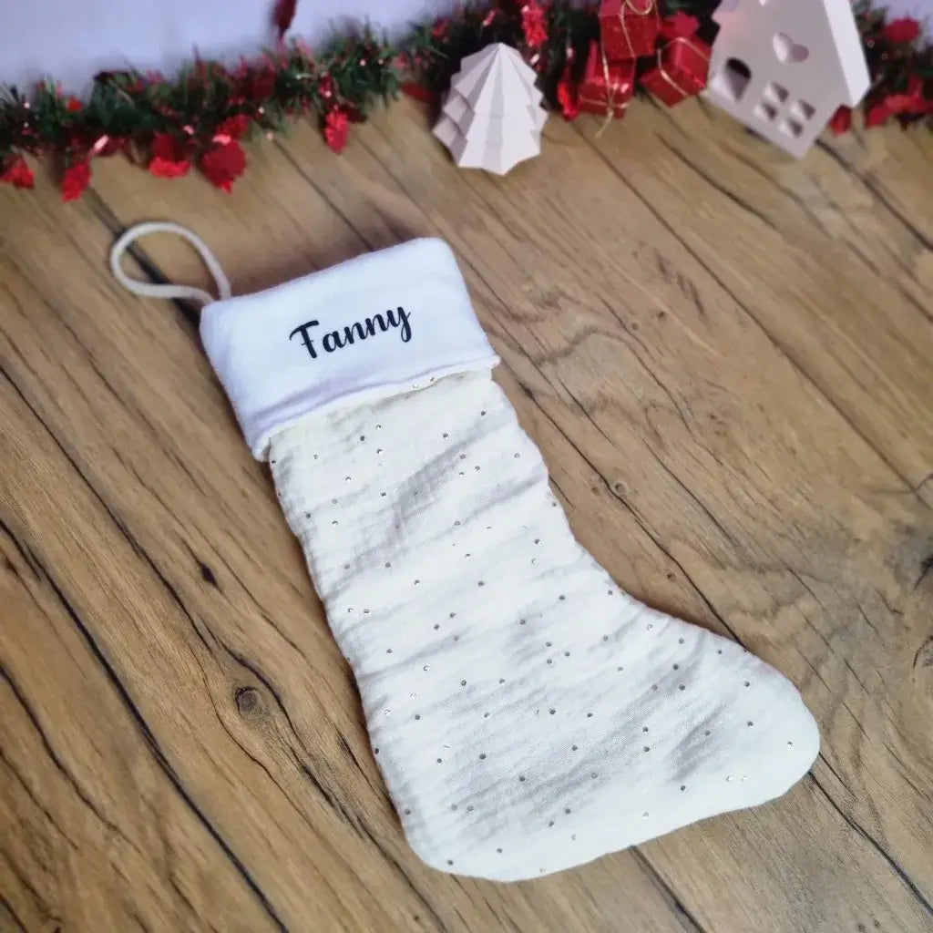 Botte de Noël à suspendre en tissu double gaze de coton blanc. Cette botte de Noël est personnalisée avec le prénom "Fanny" floqué sur la partie supérieure en polaire blanche.