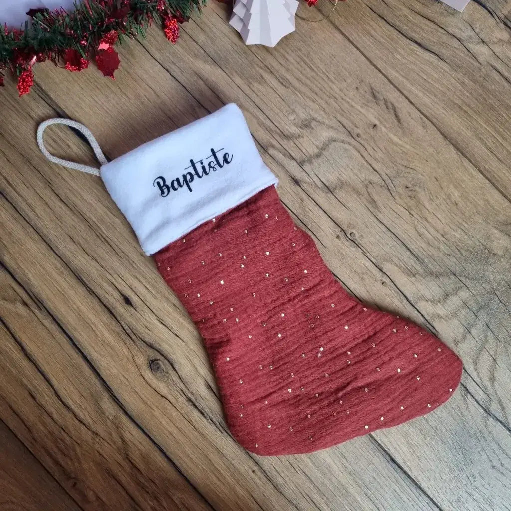 Botte de Noël à suspendre en tissu double gaze de coton rouge. Cette botte de Noël est personnalisée avec le prénom "Baptiste" floqué sur la partie supérieure en polaire blanche.