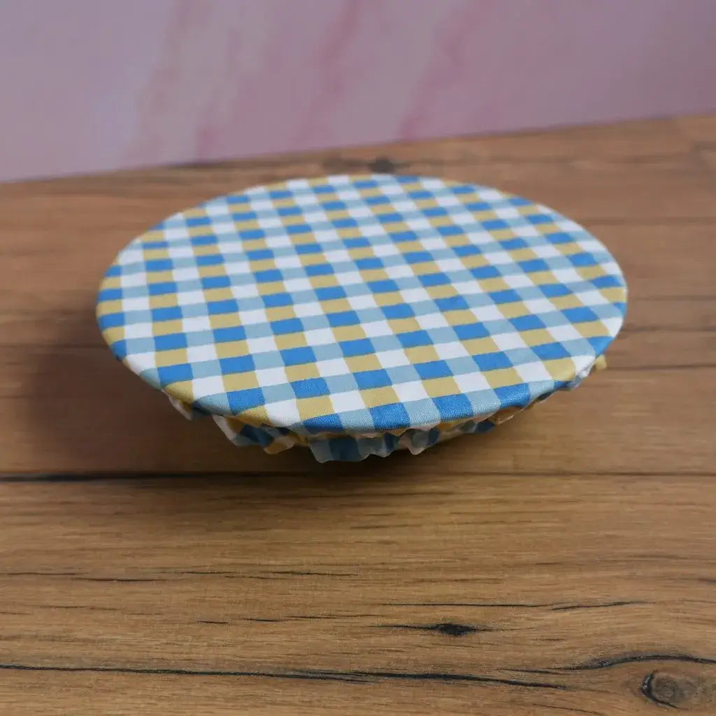 Charlotte couvre-plat ronde en coton enduit à motif carreaux bleus et jaunes, réutilisable et lavable, idéale pour couvrir un bol ou saladier sans film plastique. Couvre-aliment zéro déchet avec élastique intégré pour conserver les restes au frigo ou protéger les plats lors d’un pique-nique.