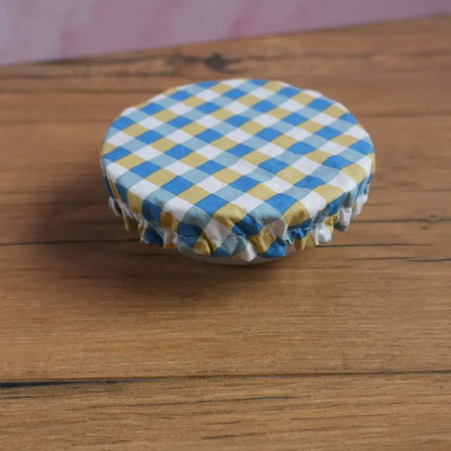Petite charlotte couvre-plat ronde en coton enduit à motif carreaux bleus et jaunes, format taille S, réutilisable et lavable, dotée d’un élastique froncé pour s’ajuster sur un bol ou ramequin. Alternative zéro déchet aux films alimentaires pour conserver les restes ou protéger un dessert maison.