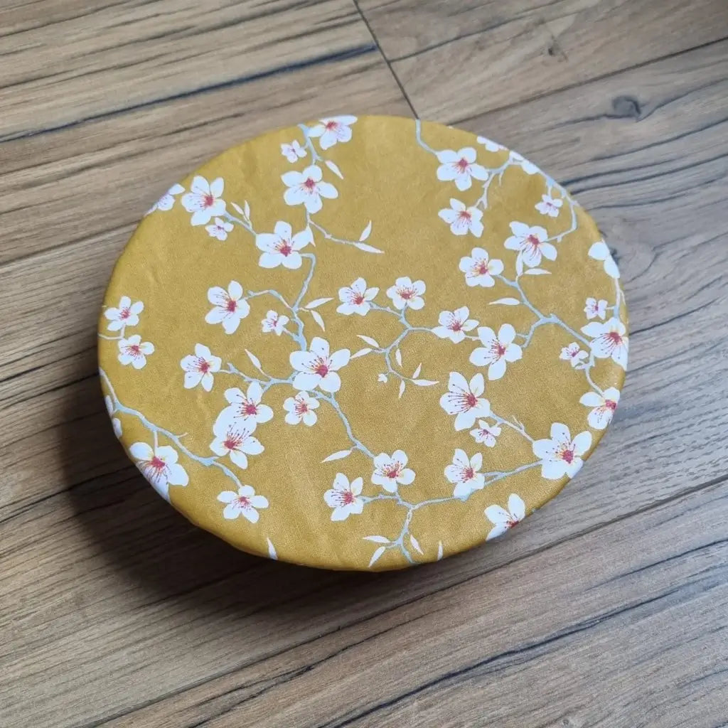 Charlotte couvre-plat rond en coton enduit réutilisable au motif fleurs jaunes. Cette charlotte alimentaire est étirée sur un bol ou une assiette creuse pouvant aller d'un diamètre de 20 à 22 cm. 