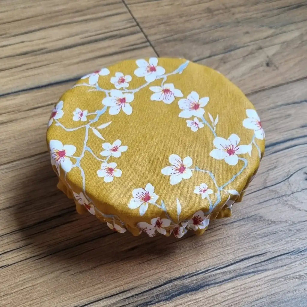 Charlotte couvre-plat rond en coton enduit réutilisable au motif fleurs jaunes. Cette charlotte alimentaire est étirée sur un bol pouvant aller d'un diamètre de 12 à 14 cm. 