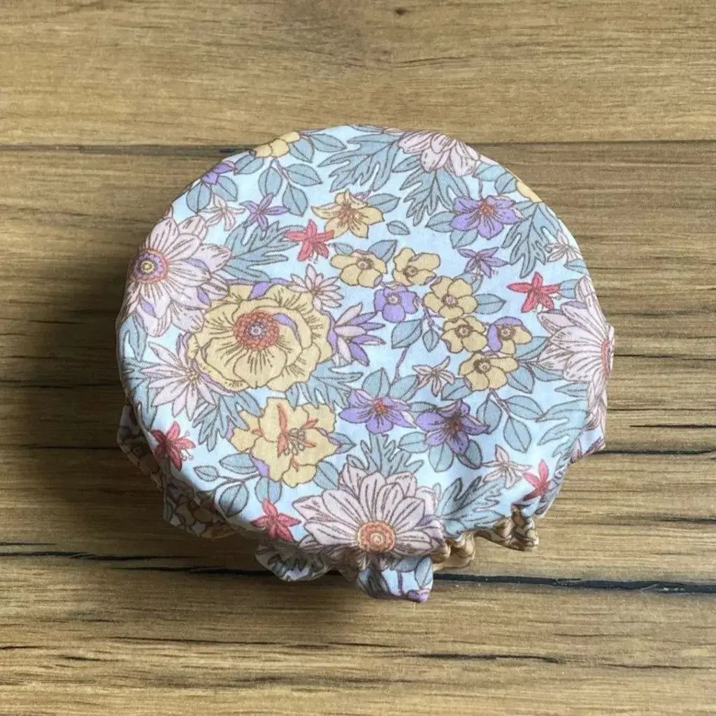 Charlotte couvre-plat rond en coton enduit réutilisable au motif fleurs mauves. Cette charlotte alimentaire est étirée sur un bol pouvant aller d'un diamètre de 12 à 14 cm. 