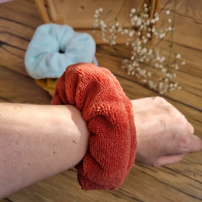 Chouchou en éponge de bambou lavable et réutilisable porté au poignet, avec d’autres chouchous en arrière-plan sur un sol en bois. Accessoire polyvalent et écologique, idéal pour attacher les cheveux ou absorber l’eau pendant la routine beauté. Modèle en tissu ultra-doux couleur terracotta, parfait pour un maintien confortable sans abîmer les cheveux. Fabrication artisanale et respectueuse de l’environnement.