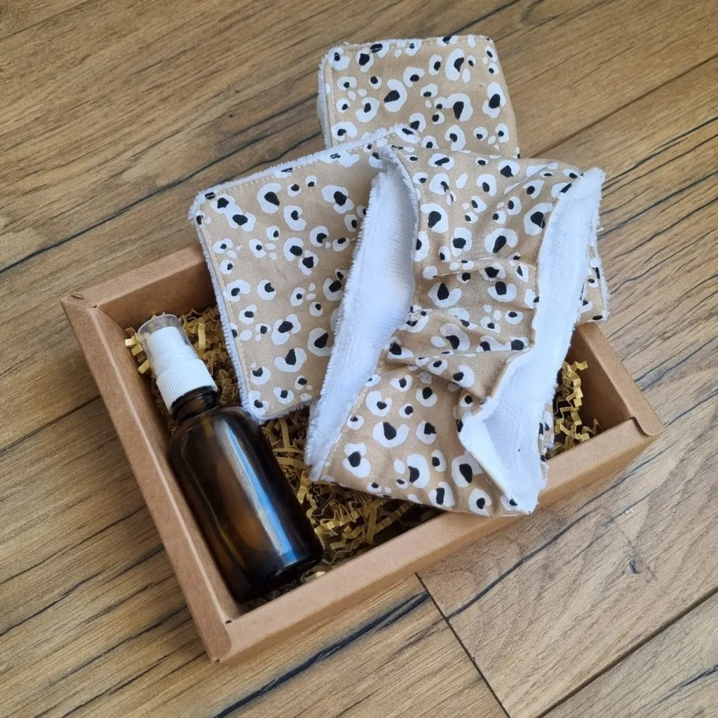 Coffret bien-être huile de soin comprenant une lingette 10x10 cm, une maxi-lingette 18x18 cm et un bandeau de soin avec une face en éponge de bambou blanc et une face en coton imprimé à motif léopard, ainsi qu'une huile de soin (amande douce ou jojoba). Le tout est présenté dans un joli coffret en carton.