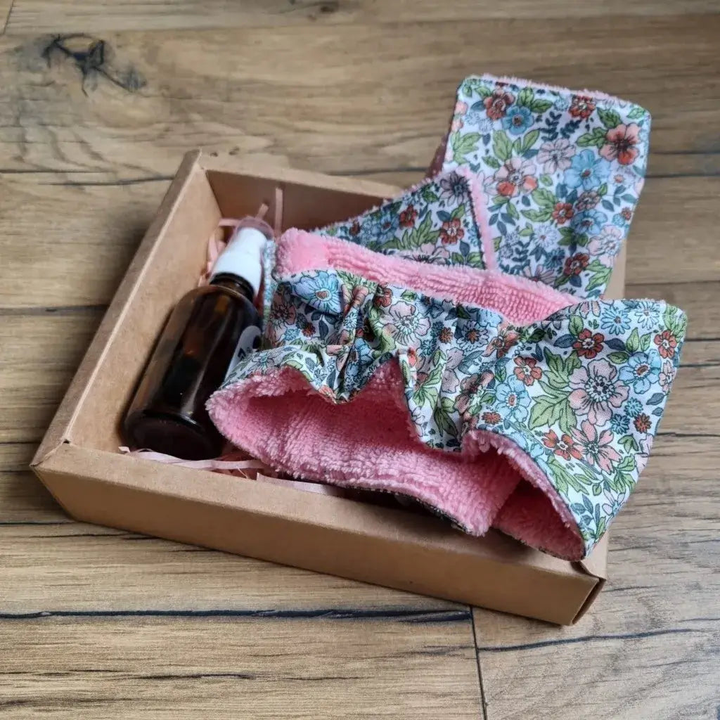 Coffret bien-être huile de soin comprenant une lingette 10x10 cm, une maxi-lingette 18x18 cm et un bandeau de soin avec une face en éponge de bambou de couleur orchidée et une face en coton imprimé à motif fleuri, ainsi qu'une huile de soin (amande douce ou jojoba). Le tout est présenté dans un joli coffret en carton.