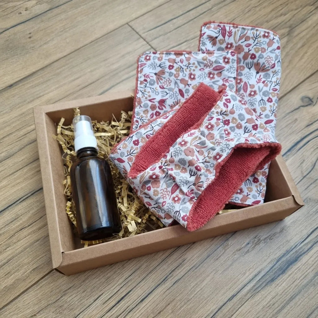 Coffret bien-être huile de soin comprenant une lingette 10x10 cm, une maxi-lingette 18x18 cm et un bandeau de soin avec une face en éponge de bambou de couleur terracotta et une face en coton imprimé à motif liberty, ainsi qu'une huile de soin (amande douce ou jojoba). Le tout est présenté dans un joli coffret en carton.