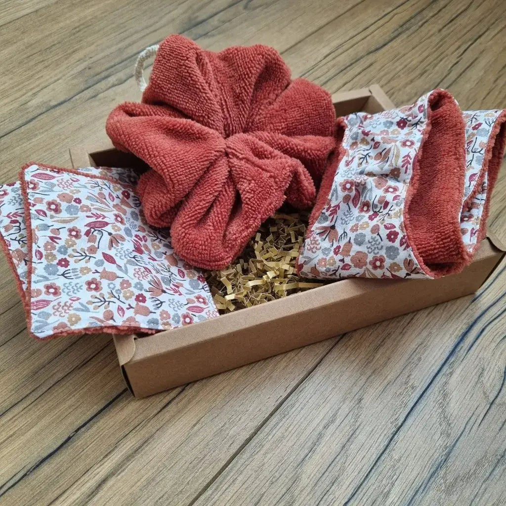 Coffret cadeau bien-être salle de bain comprenant une fleur de douche en éponge de bambou de couleur terracotta, une petite lingette en éponge de bambou terracotta doublée d'un tissu en coton imprimé à motif liberty, la même lingette au format maxi et un bandeau de soin également en éponge de bambou terracotta et doublé avec le même tissu à motif. le tout est disposé dans un joli coffret en carton.