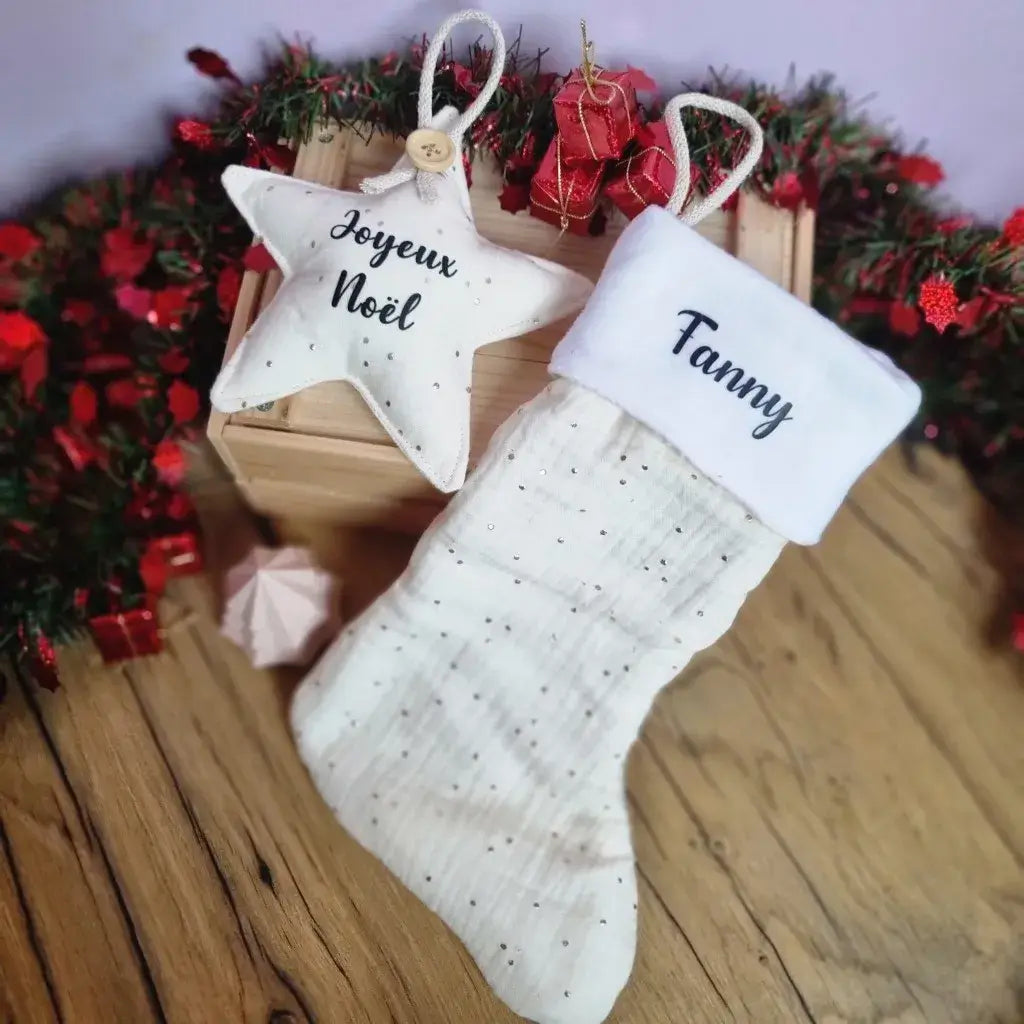 Combo étoile de Noël et botte de Noël à suspendre en tissu double gaze de coton blanc. La botte de Noël est personnalisée avec le prénom "Fanny" floqué en noir sur la partie supérieure de la botte en tissu polaire blanc. L'étoile quant à elle est personnalisée avec l'inscription "Joyeux Noël" floquée en noir en son centre.