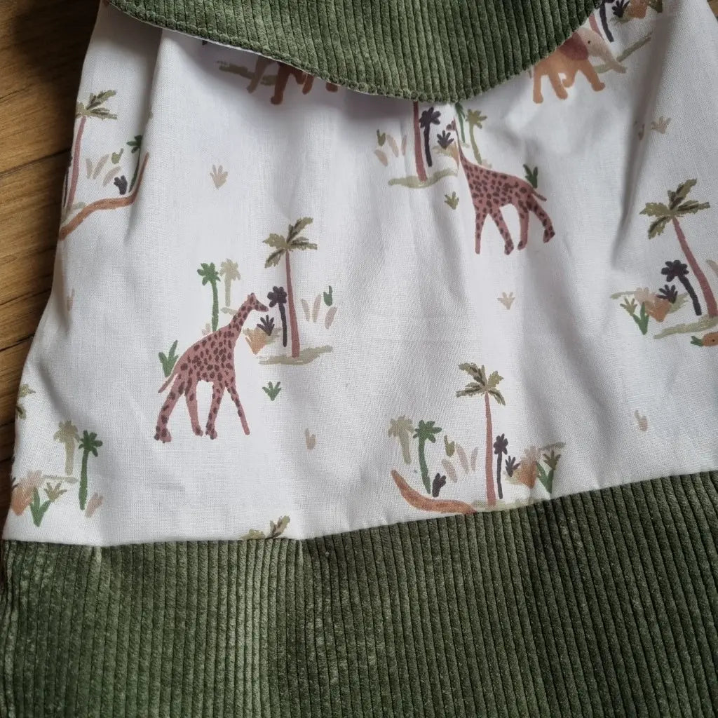 Zoom sur un sac pochon pour enfant pour montrer en détail le motif savane qui compose le tissu principal de ce sac. On aperçoit une partie de la base et du rabat du sac en velours côtelé vert foncé.