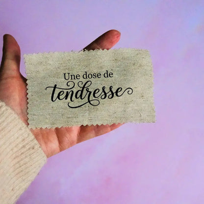 Étiquette en tissu personnalisée avec inscription floquée Une dose de tendresse tenue à la main pour création artisanale