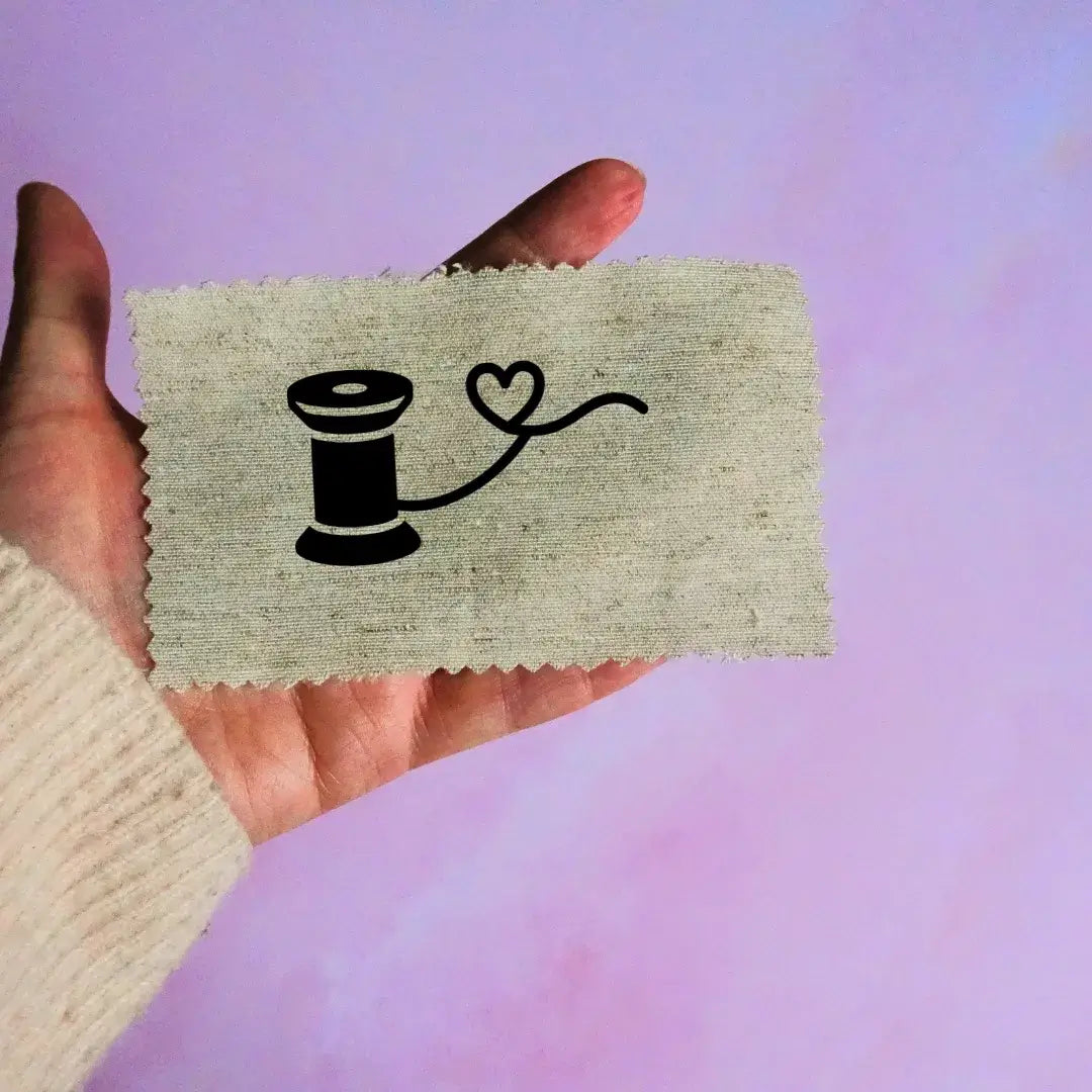 Étiquette en tissu personnalisée avec un dessin floqué d'une bobine de fil tenue à la main pour création artisanale