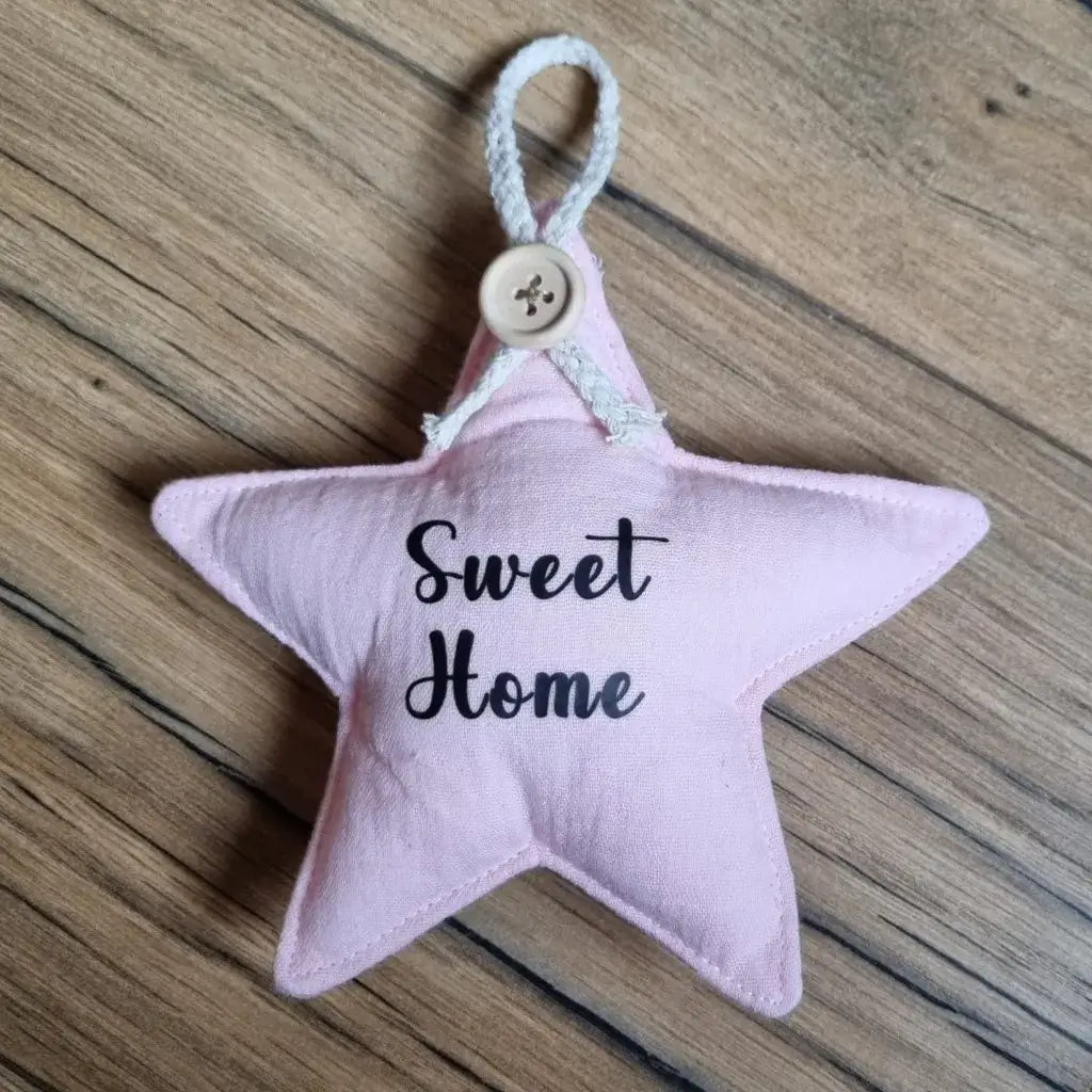 Etoile en tissu double gaze de coton de coloris rose pâle. Cette étoile peut se suspendre à l'aide d'une petite cordelette en coton maintenue avec un ravissant petit bouton. Cette étoile est personnalisée avec l'inscription "Sweet Home" floquée à l'écriture noire en son centre.