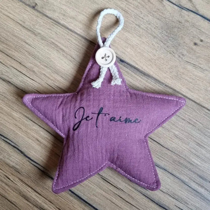Etoile en tissu double gaze de coton de coloris violet. Cette étoile peut se suspendre à l'aide d'une petite cordelette en coton maintenue avec un ravissant petit bouton. Cette étoile est personnalisée avec l'inscription "Je t'aime" floquée à l'écriture noire en son centre.