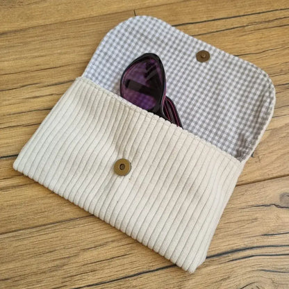 Etui à lunettes en velours côtelé de coloris beige. Cet étui est ouvert. Une paire de lunettes de soleil est à moitié glissée à l'intérieur. On distingue la doublure de cet étui à lunettes en coton imprimé à motif carreaux beiges.