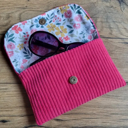 Étui à lunettes cousu main en velours côtelé framboise avec intérieur en coton fleuri, bouton pression doré et finitions soignées, parfait pour protéger vos lunettes de soleil ou de vue avec élégance. Accessoire artisanal chic et coloré, alliant douceur du tissu et praticité au quotidien.
