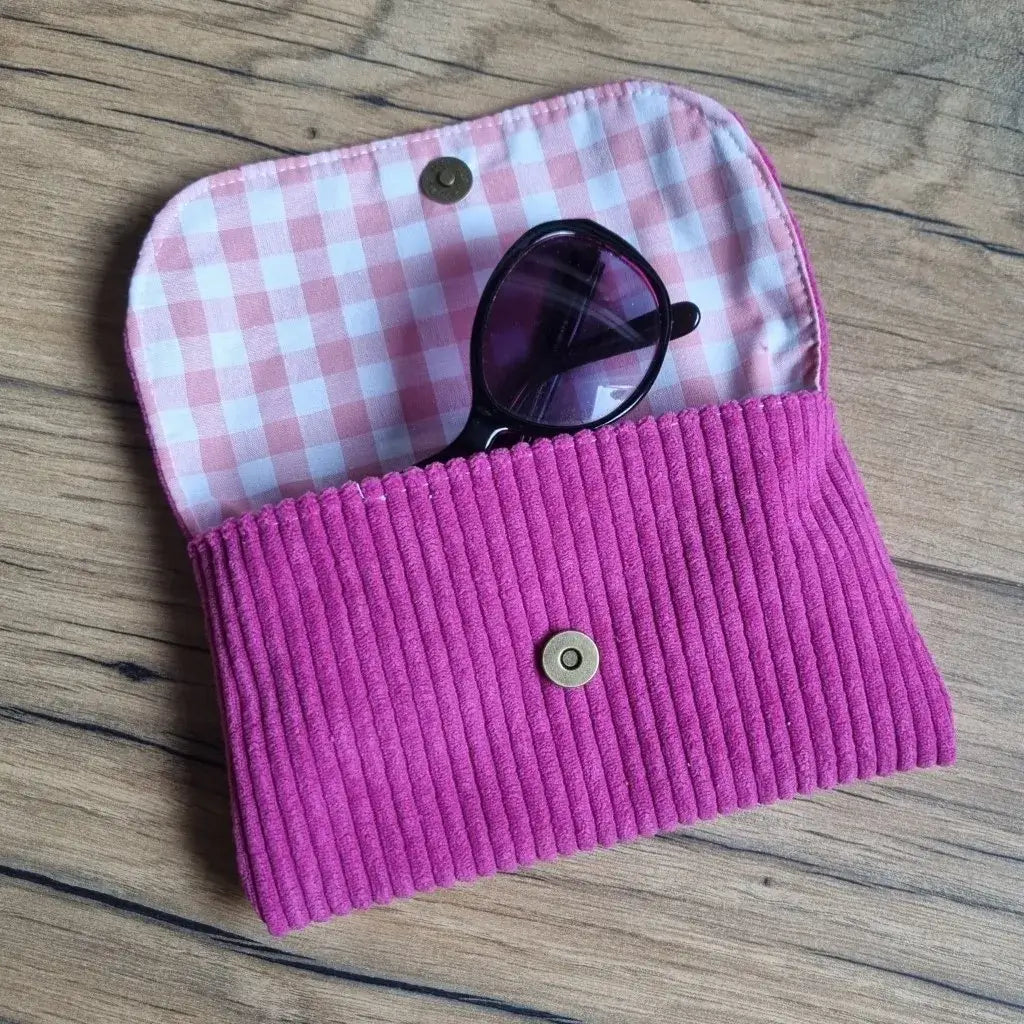 Étui à lunettes fait main en velours côtelé magenta, doublé d’un tissu à carreaux roses et blancs. Accessoire élégant et pratique pour protéger vos lunettes de soleil ou de vue dans un écrin doux et coloré. Fermeture à bouton pression doré, parfait mélange entre style rétro et touche artisanale raffinée.