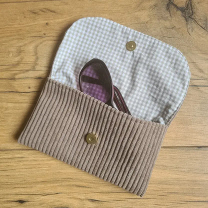 Etui à lunettes en velours côtelé de coloris taupe. Cet étui est ouvert. Une paire de lunettes de soleil est à moitié glissée à l'intérieur. On distingue la doublure de cet étui à lunettes en coton imprimé à motif carreaux beiges.
