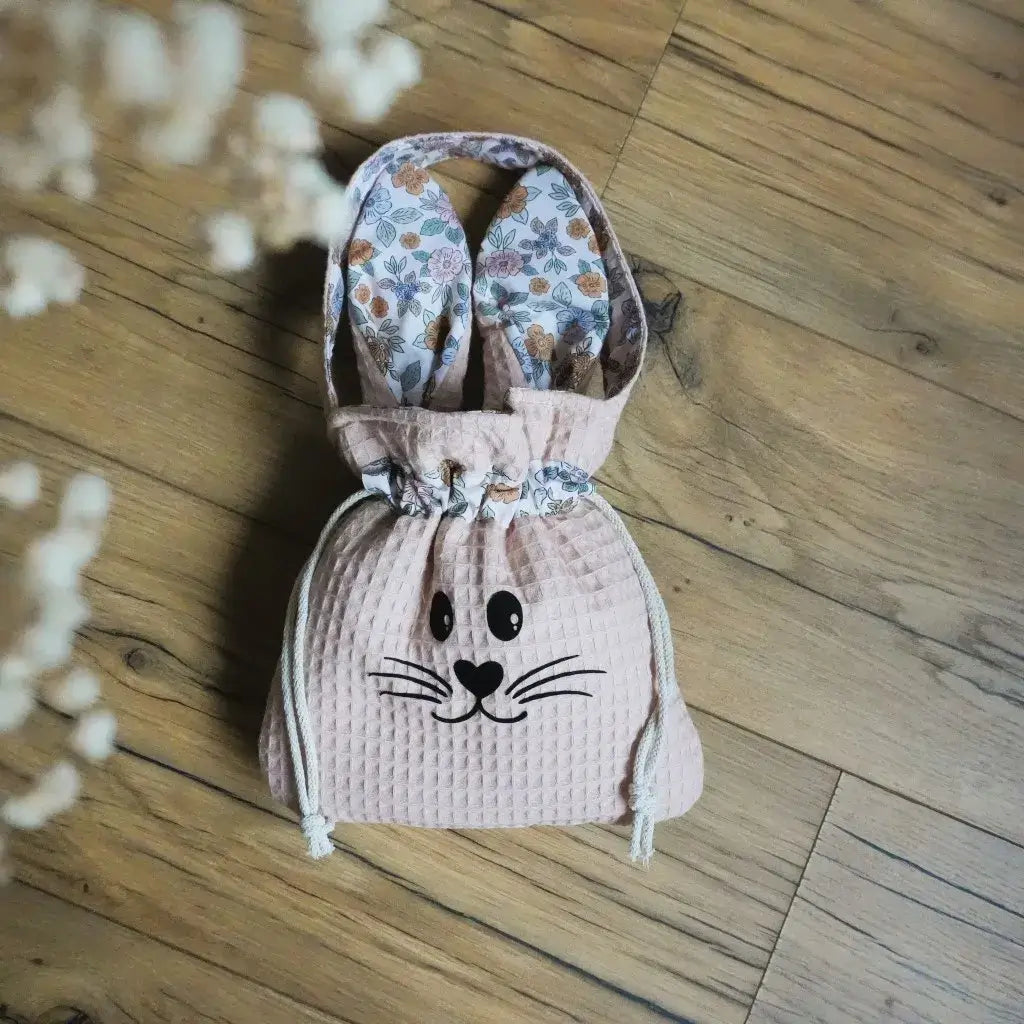 Pochon en nid d'abeille coloris peau avec flocage lapin noir, oreilles doublées de tissu floral, posé sur un parquet bois.